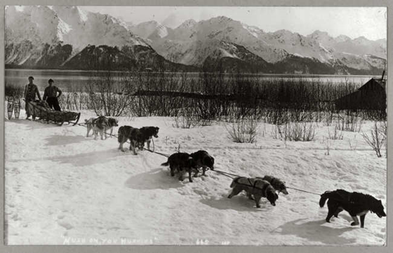 Dog team pulling a sled through a snow-covered field, with two men with snow shoes posed behind; snow-covered mountains and placid lake in background. Frank and Frances Carpenter Collection — Lib. of Congress Prints and Photographs Division Dog team pulling a sled through a snow-covered field, with two men with snow shoes posed behind; snow-covered mountains and placid lake in background. Frank and Frances Carpenter Collection — Lib. of Congress Prints and Photographs Division